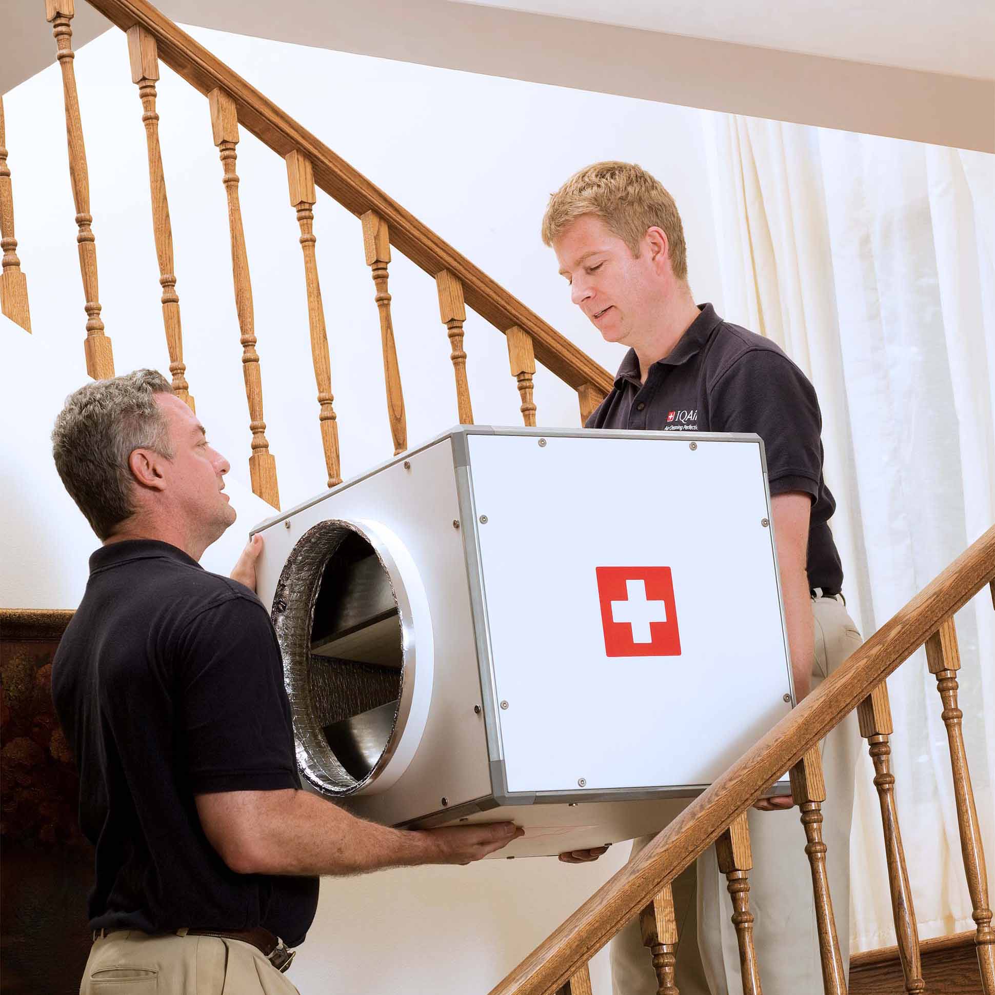 Gabinete de filtración HVAC PerfectPro IQAir transportado por instaladores durante la instalación en una vivienda.